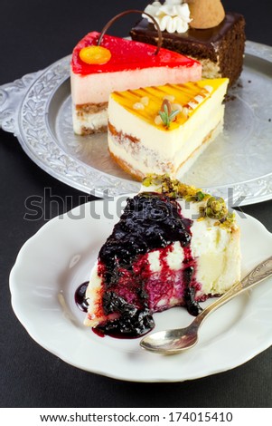 Slice of delicious cheesecake with blueberry syrup on a white plate on a black background
