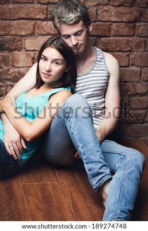 young couple in love sitting on the floor against a brick wall