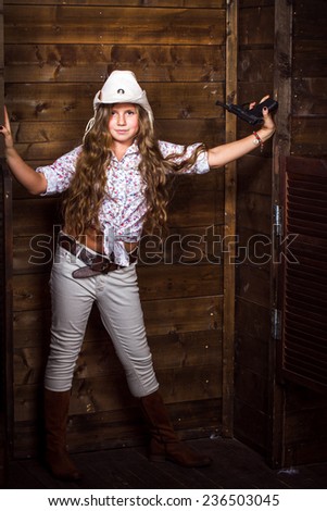 Cute teenager girl in a cowboy hat on a ranch posing with toy gun