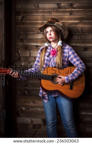 Cute teenager girl in a cowboy hat on a ranch and plays the guitar