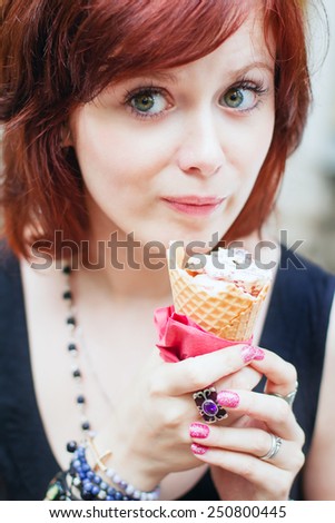 Young pretty girl with ginger hair eating ice cream in wafer cone