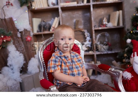 active, cheerful kid is sitting in a chair near the Christmas tree
