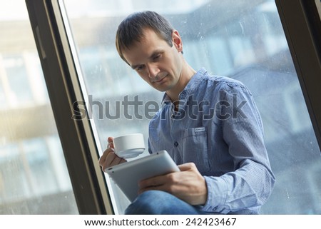 businessman with a cup of coffee and with the tablet at the window
