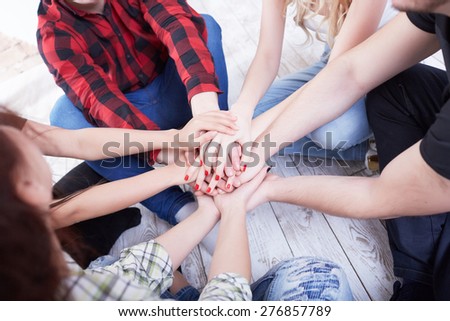group of students in a bright room on the floor sit in a circle holding hands