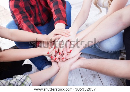 group of students in a bright room on the floor sit in a circle holding hands
