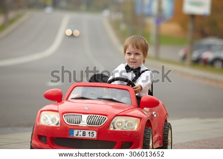 year-old boy in a white shirt in a red toy car in the street