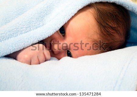 Beautiful white baby boy with big eyes is lying under blanket