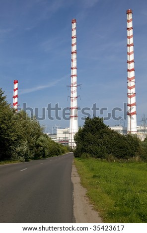 Industry in nature, red and white chimney against green grass, blue sky