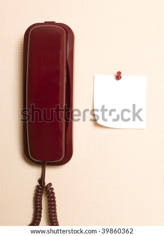 Red telephone is hanging on light brown wall