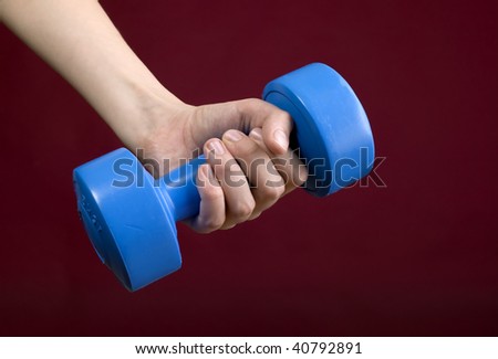 Human hand is holding blue dumbbell, red background
