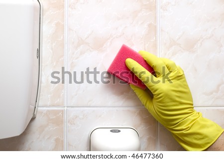 Cleaner is cleaning tiles in bathroom with red sponge