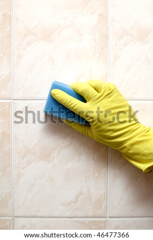 Cleaner is cleaning tiles in bathroom with blue sponge