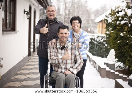 Happy disabled young man with palsy in wheelchair surrounded by father and mother, laughing