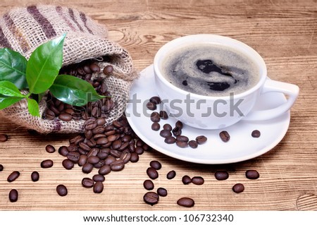 Cup of coffee with coffee beans in a beautiful brown bag, green branch of a coffee plant