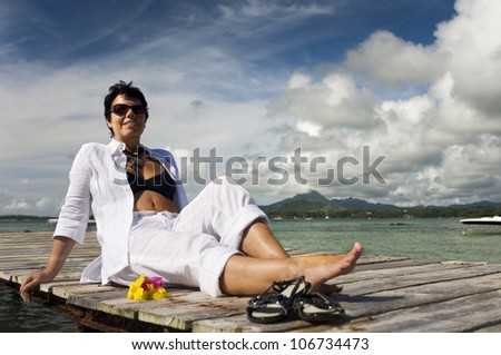beautiful mature woman wearing white linen clothing and sitting on a boardwalk, relaxing in holidays in Mauritius
