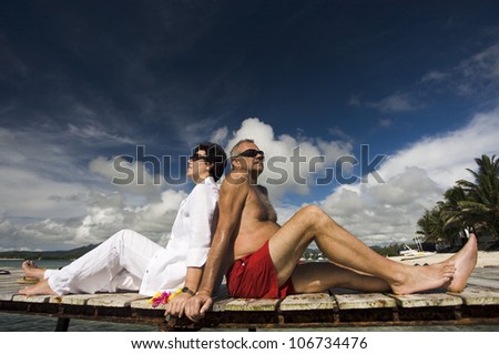 happy mature couple sitting back to back on a boardwalk, relaxing in holidays in Mauritius