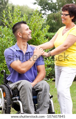 disabled young man in wheelchair and a mature woman touch his hand, care for a wheelchair user