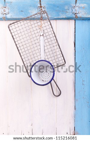 cookware set over blue and white wooden wall with old fashioned metal hanger  (Metal net seamless, iron enameled colander)