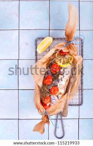 baked Gilthead fish in baking paper garnished with vegetables, herbs and lemon on a blue tiled kitchen worktop, Sea Bream fish
