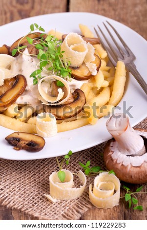 Schupfnudeln (Swabian potato noodles from Southern Germany) with mushroom sauce, fresh brown mushrooms, herbs and parmesan cheese on a white plate on wooden board