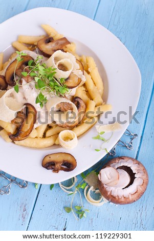 Schupfnudeln (Swabian potato noodles from Southern Germany) with mushroom sauce, fresh brown mushrooms, herbs and parmesan cheese on a white plate on blue wooden table