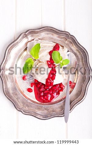 Lovely ruby-red pomegranate fruit over vanilla ice cream with mint leafs on a silver plate, bird\'s-eye view