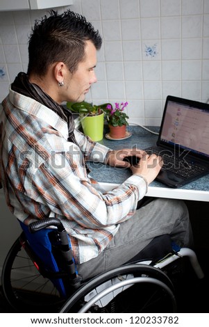 young man in wheelchair in Barrier-free apartment is using his laptop, disabled young man is surfing in internet