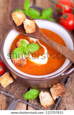 fresh tomato soup with basil thyme and raw tomatoes with bread pieces in a bowl on wooden table, ready to eat