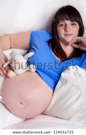 Pregnant woman relaxing at home on the couch with stuffed animal for the newborn