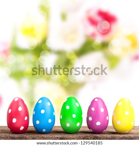 5 colorful easter eggs on a row on wooden table with fresh tulips in background