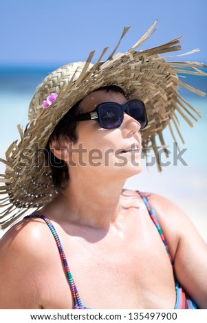 happy mature woman with sun hat and sun glasses is relaxing at the beach