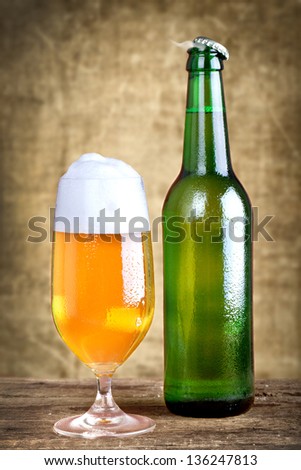 Frosty fresh beer with foam in a glass and in a bottle with rustic background