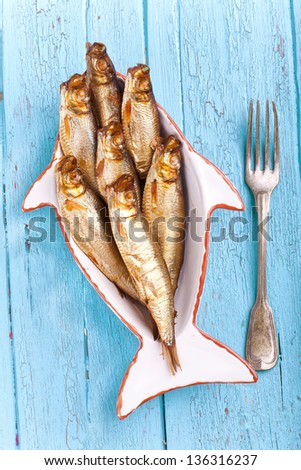 golden brown smoked sprats in a bowl fish shaped with a fork on blue wooden table, ready to eat