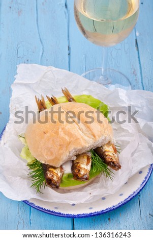 bread roll served with sprats and salad, Healthy sprats salad sandwich on a bread roll on blue wooden table with a glass of white wine