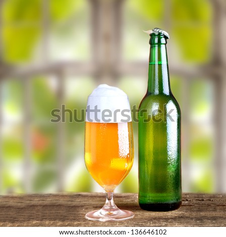 fresh cold beer in a glass and in a bottle on rustic wooden table with natural background outside the window