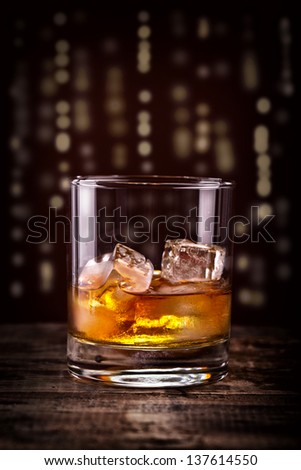 Scotch on wooden table with lightning skyline background, An old and vintage counter top with highlight and a glass of hard Liquor, Whisky or Whiskey and ice