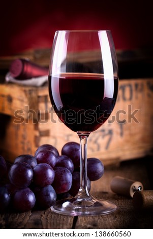 a glass of red wine with fresh blue grapes on old rustic wooden table with a wine bottle in an old wooden box in background