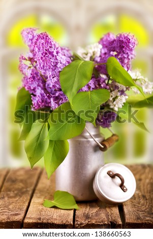 a fresh bouquet of lilac or elder with green leafs in a rustic jug on wooden table with natural background