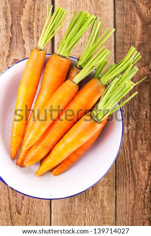 freshly cleaned carrots in a bowl on wooden table, bird`s eye view