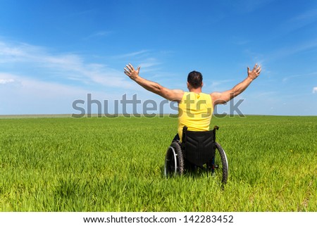 Happy Handicapped Man On A Wheelchair Over A Green Meadow, Looking For Freedom