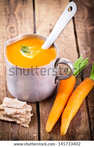 fresh carrot soup in a old rustic Cup with spoon and fresh carrots on wooden table