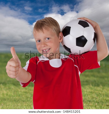 laughing young boy with soccer ball and red soccer dress with natural soccer background