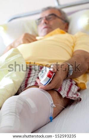 Knee surgery after operation patient senior man on the bed in Hospital, room at hospital with Equipment, man`s Hand is pressing emergency nurse call button
