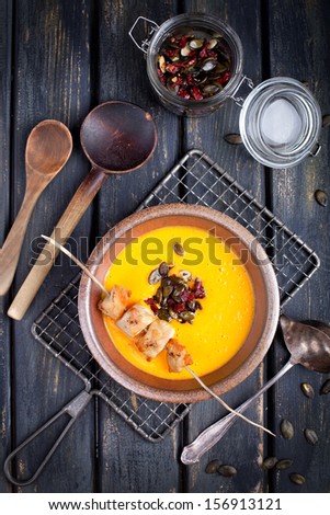 delicious pumpkin soup with chicken, pumpkin seeds and cranberries on rustic wooden board