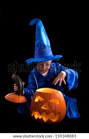 boy in blue witch\'s hat and costume with big pumpkin, a little wizard on Halloween isolated on black