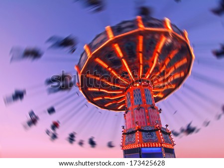 colorful carousel in motion with sundown in background, people enjoy their ride in the carousel