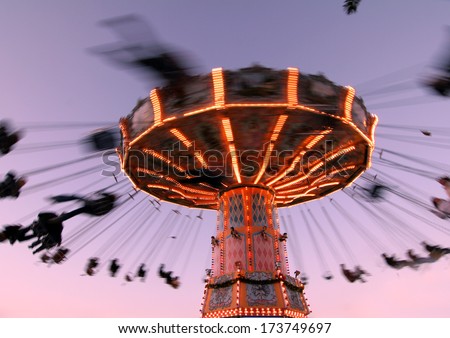 Colorful Carousel In Motion With Sundown In Background, People Enjoy Their Ride In The Carousel