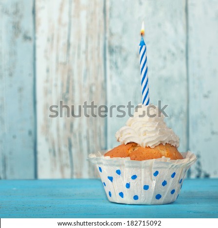 cream birthday cupcake with candle on blue wooden background