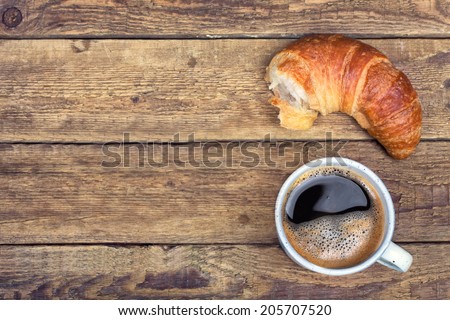 Coffee and croissant for breakfast on rustic wooden table, top view