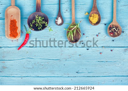 Colorful Spices and herbs on rustic spoons over blue wooden background